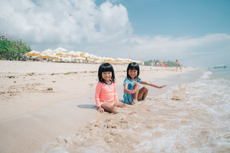 two little girls sitting on the sand waiting for the waves to come