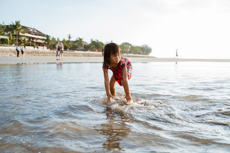 little girl bent over and playing sand on the beach