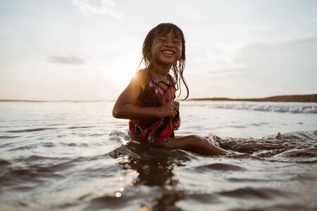 Asian little girl sitting on sand in the beach while playing waterの写真素材