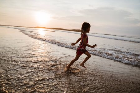have fun little Asian girl running while enjoying the beautiful beachの写真素材