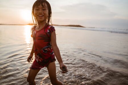 Little girl running on the beach while playing waterの写真素材