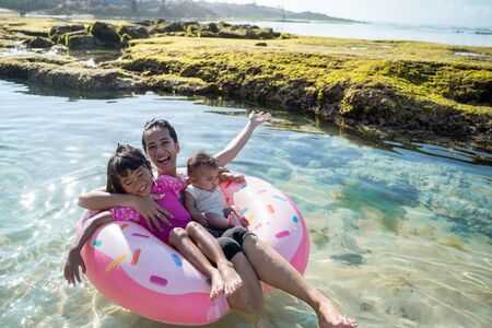 asian mother and her two children laugh while riding on the buoy ringの写真素材