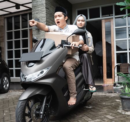 Asian Muslim couples with motorbike mudik carrying lots of itemsの写真素材