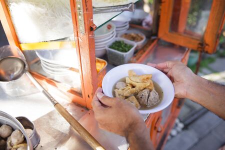 street food vendor pouring soup into a bakso meatball bowlの写真素材