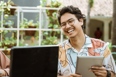 bespectacled youth laughs holding a tablet