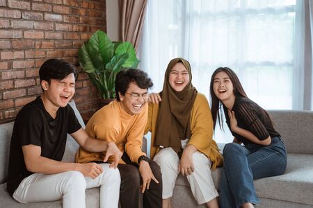 group of Asian young people sitting together on the couch laughing togetherの写真素材