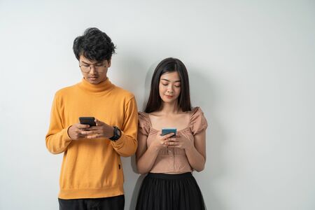 Asian young couples use their smart phones while standingの写真素材