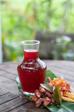 fresh red ginger drink in a glass bottle with shaved secang wood, red ginger, lemongrass, cloves, orange leaves on a wooden tableの写真素材