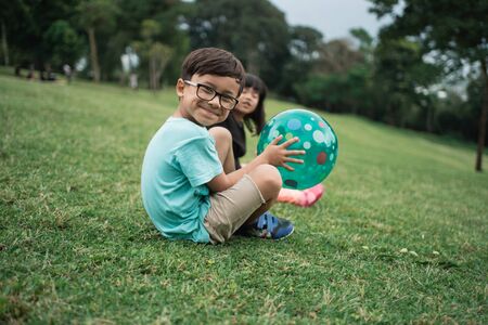 boy holding the ball sits on the grass fieldの写真素材