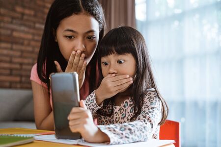 kid and sister shocked while looking at phoneの写真素材