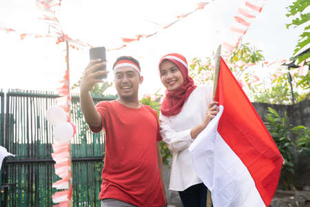 young couple take selfies with cameras while wearing red and white attributesの写真素材