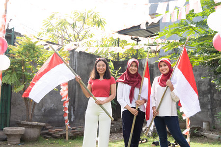 three girls in red and white shirts and headbands stand holding bamboo sticks with Indonesian flags