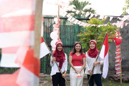 three Asian girls wearing red and white attributes and carrying Indonesian-flagged bamboo sticksの写真素材