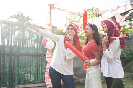 three cheerful girls wearing red and white clothes are taking selfies together using cellphonesの写真素材