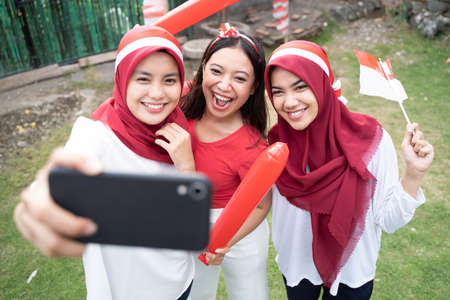 young girls laugh cheerfully taking selfies using red and white attributes with smartphonesの写真素材