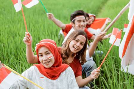close up of young men and women hold and wave the Indonesian flag while wearing red and white...