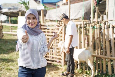 muslim woman with scarf showing thumb up while standing in the goat farmの写真素材