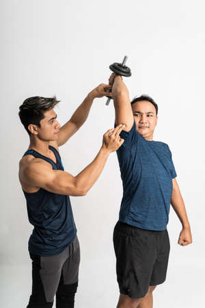 trainer accompanies a man lifting dumbbell for triceps exercises with holding hand to make the right movesの写真素材