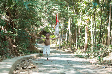 asian little boy running without clothes when holding the red and white flag and raisedの写真素材