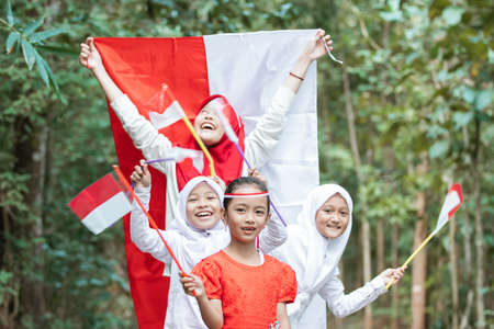 smilling little girls stand in line when holding and fly the flag together to celebrating Indonesian independence dayの写真素材