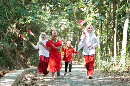 group of little girls running chasing each other when holding small the red and white flag and raised the flag togetherの写真素材