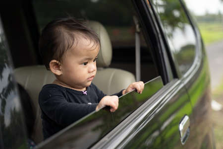 cute baby looks outside while standing in the car with the windows openの写真素材