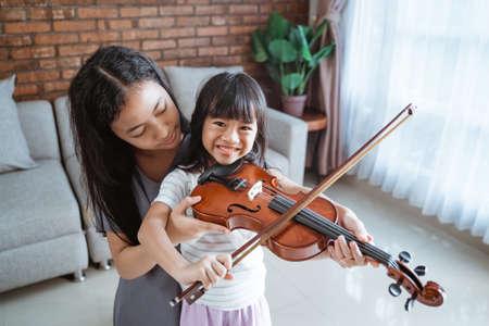 little girl smile as teenage girl help a child hold the violin properlyの写真素材