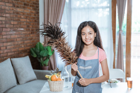 teenage girl wearing a smiling apron while holding a feather duster looking at the camera