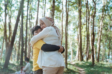 veiled mother and son are happy and hug as they stand among the treesの写真素材