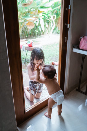 Two Asian siblings smiled at each other through the window glass