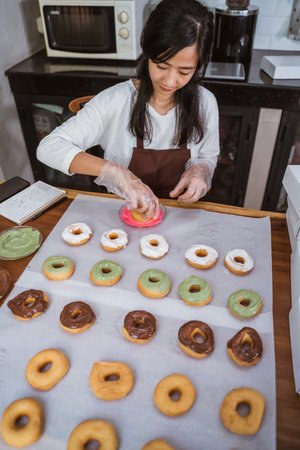 beautiful women wearing aprons and gloves while decorating various donuts with chocolate frosted