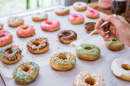 close up of hands decorating various donuts with chocolate frosted, pink glazed and donut sprinkleの写真素材