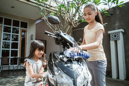 potrait happy young girl and little girl washing motorcycleの写真素材