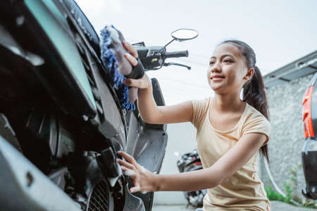 asian young girl washing his motorcycle scooter with soap and spongeの写真素材