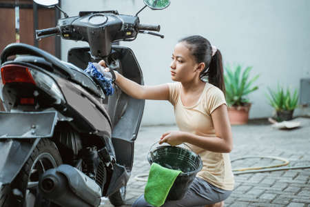 asian young girl washing his motorcycle scooter with soap and spongeの写真素材