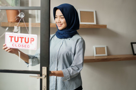 cheerful woman in closed sign and smiling while standing against front door