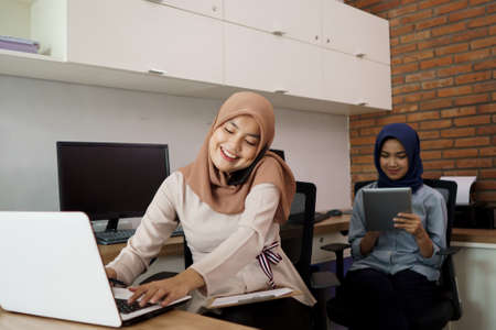 portrait of a beautiful muslim woman who is very happy and busy workingの写真素材