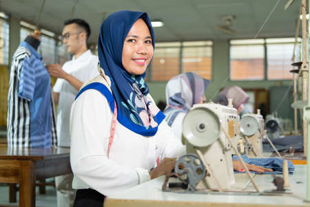 female tailor in hijab smiles look at camera with a measuring tape worn around her neck usingの写真素材