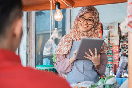 veiled girl seller the cart shop smiles using tablet pc when serving customerの写真素材