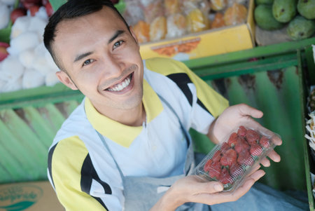 Smiling male salesman carrying a packet of strawberries in two hands