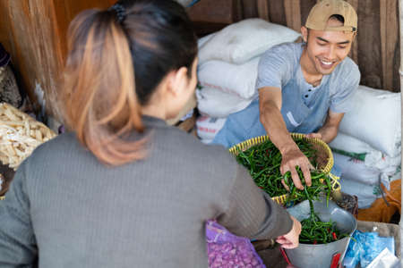 male sellers pick up green chilies to be weighed serving female buyersの写真素材