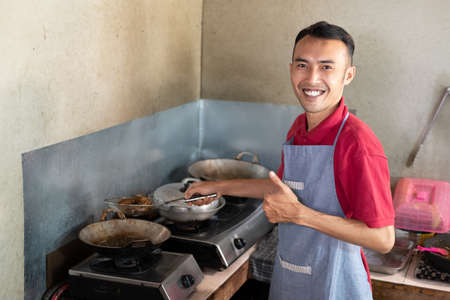 the male waiter smiles with a thumbs up while frying side dishes for customersの写真素材