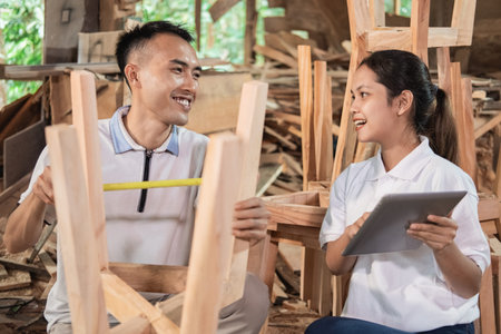 furniture business woman uses a tablet when talking to a carpenter who measures wood