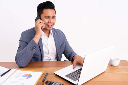 An attractive and cheerful young business man holding a cellphone and smiling while sitting down.の写真素材