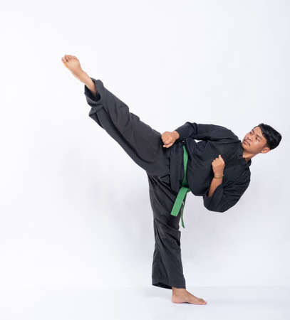 view side of man with one leg kicking upwards while wearing a pencak silat uniform with a green beltの写真素材