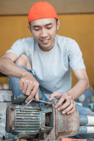 asian male electronics worker use three head wrench to repair water pump machineの写真素材