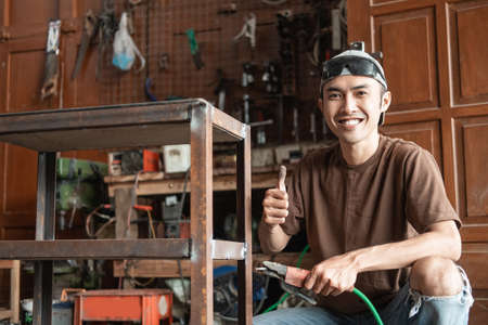 close up of Male welder smiling with a thumbs up while holding an electric welderの写真素材