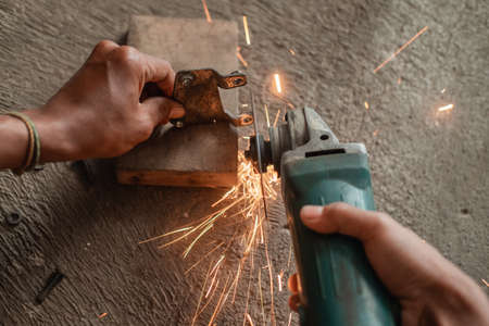 close up of welders hand using a grinder to smooth the surface of the iron hingeの写真素材