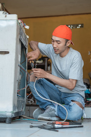 Asian electronics workers use pliers to fix a washing machine cable that broke while squatting