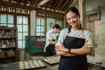 Smiling asian girl in apron looking to the camera with baking sheet cake backgroundの写真素材